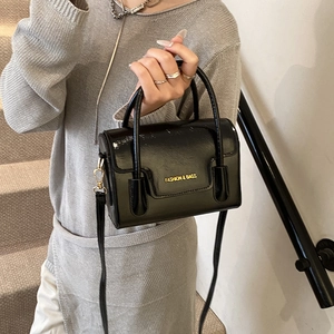 Glossy black mini handbag with gold lettering shown in a modern staircase setting
