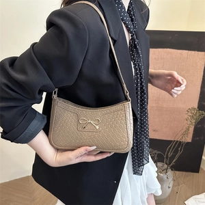 Chic khaki woven embossed shoulder bag with a gold bow buckle worn with a black suit
