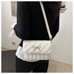 Close-up of a white quilted shoulder bag featuring a gold bow buckle and strap details