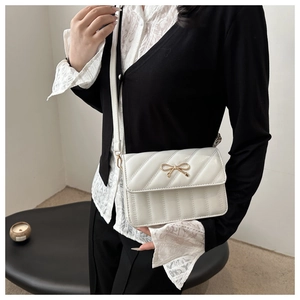 Macro detail of white quilted crossbody bag with a golden bow and sleek leather strap