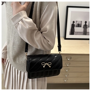 Détail du sac matelassé noir brillant avec boucle nœud dorée élégante et bandoulière