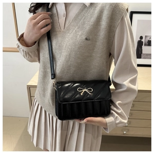 Detail shot of black PU leather shoulder bag featuring a golden metal bow and quilted texture