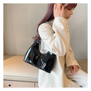 Glossy black patent leather crescent shoulder bag styled with a minimalist beige suit jacket