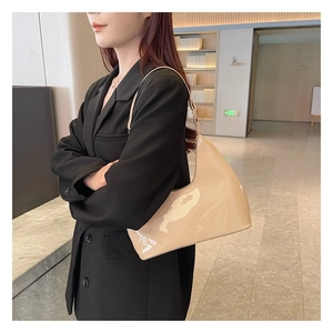 Glossy beige patent leather hobo bag worn by a model in a modern professional setting