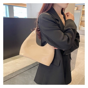Close-up of a beige glossy patent leather shoulder bag worn by a model in a hobo style