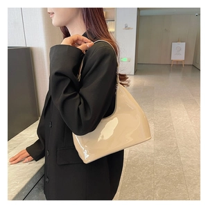Detail of glossy beige patent leather underarm bag on model with black blazer