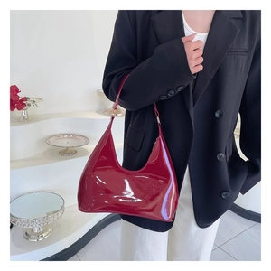 Close-up of a glossy deep red patent leather hobo bag styled on a model's shoulder