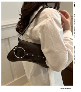 Détail du sac baguette marron foncé avec boucles et rivets argentés porté par un mannequin