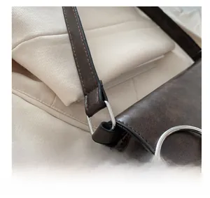 Détail de la boucle en métal argenté et de la bandoulière en cuir marron foncé du sac