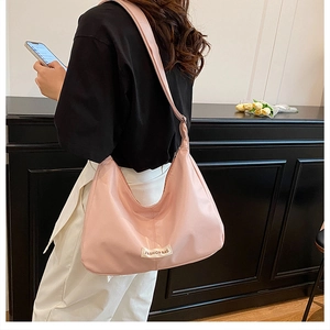 Detail of pink crescent shoulder bag featuring a fashion logo tag and wide strap