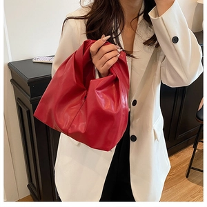 Detail of red pleated cloud bag made of soft PU leather held by a model in a white suit