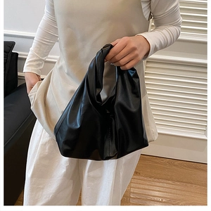 Detail of minimalist black cloud bag with knotted handle and pleated leather texture