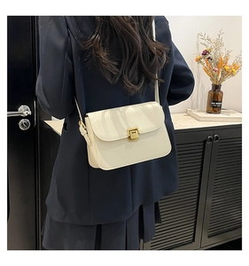 Detail of cream white leather shoulder bag with a square gold clasp on a model