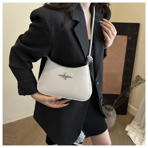 Detailed view of white woven crossbody bag with silver star charm worn by a model