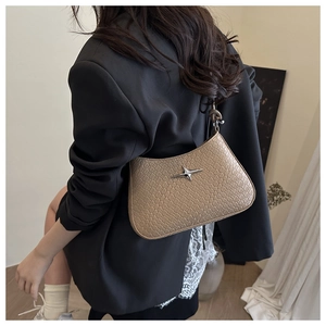 Detail of beige crocodile embossed underarm bag with silver star hardware on a model