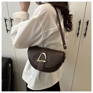 Detail of dark brown saddle bag with large gold buckle worn on the shoulder by a model