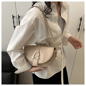 Detail of a creamy beige saddle bag featuring a large golden horseshoe hardware buckle