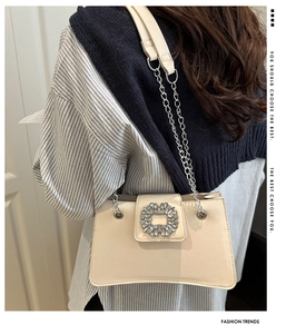 Detail view of cream leather shoulder bag with crystal buckle and metal chain strap