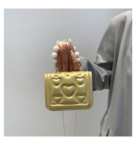 Detail of champagne gold mini bag with heart embossing and faux pearl handle strap