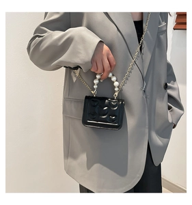 Detail of black mini handbag featuring pearl handle, gold chain and heart embossed patterns
