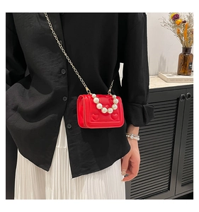 Detail of red quilted heart mini bag with white pearl handle and gold chain strap