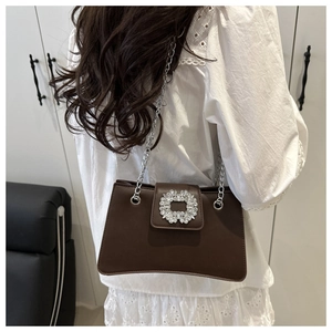 Detail of a dark brown leather shoulder bag featuring a crystal-embellished buckle and chain