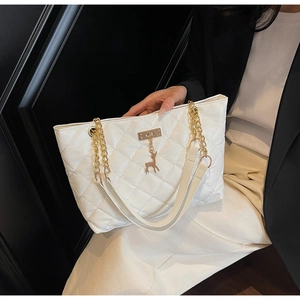Detail of white quilted tote bag featuring gold chain strap and deer pendant