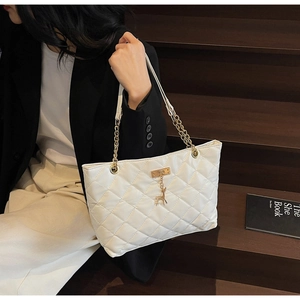 Close-up of white quilted tote bag featuring gold deer charm and chain strap detail