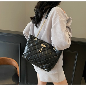 Detail of black quilted shoulder bag featuring gold chain strap and deer charm