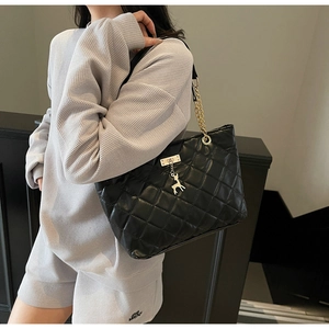Detail of black quilted tote bag with silver deer charm and chain leather strap on model