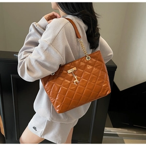 Detailed view of brown quilted tote bag featuring golden chain strap and deer charm
