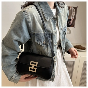 Detail of a minimalist black crossbody bag with a gold buckle on a casual denim outfit