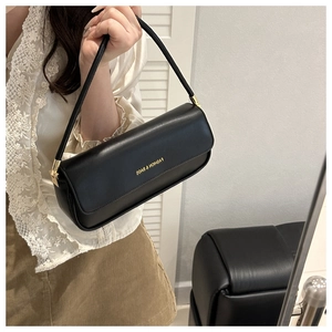 Detail of a black matte leather baguette bag with gold FASHION & BAGS lettering and hardware