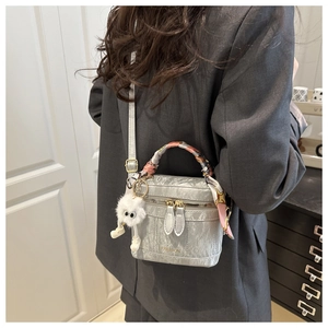 Detail of silver pleated vanity bag featuring a silk scarf handle and plush charm