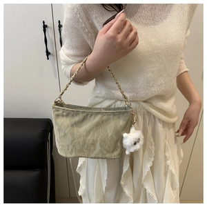 Close-up of light green textured shoulder bag with golden chain and white plush cat charm