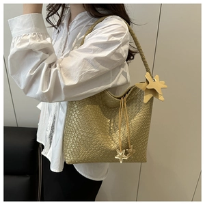 Sac fourre-tout doré tressé avec breloques étoiles porté à l'épaule par un mannequin