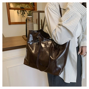 Close-up of a large dark brown patent leather tote bag on a model in a cozy cafe setting