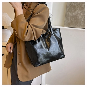 Glossy black tote bag with double shoulder straps shown on a model in a modern room
