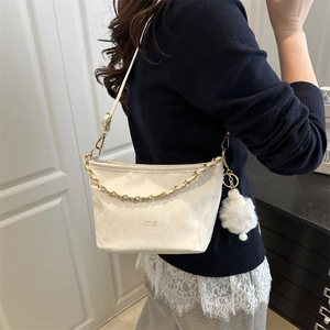 Sac seau blanc chic avec chaîne dorée et pompon en peluche, porté à l'épaule