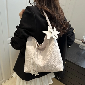 Sac fourre-tout tressé blanc crème avec pendentif étoile porté par un mannequin chic