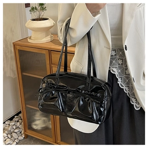 Chic black glossy leather tote bag with bow detail worn by a model in casual office attire