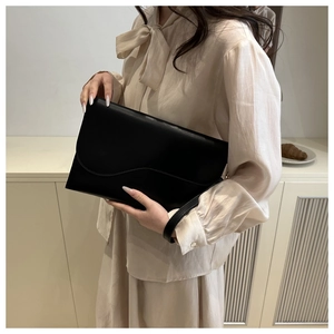 Close-up of black leather envelope clutch featuring a unique wave-shaped curved flap and wristlet