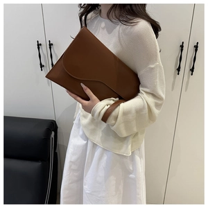 Detail view of dark brown leather clutch bag with magnetic flap and wrist strap strap