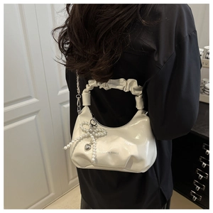 Détail du sac blanc brillant avec nœud en perles et pendentif cœur argenté