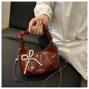 Détail du sac croissant en cuir verni bordeaux avec nœud en perles et bandoulière