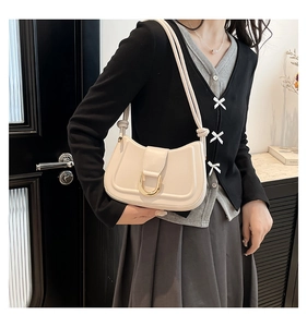 Detail of a beige crescent underarm bag featuring a gold horseshoe buckle and U-shaped stitching