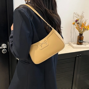 Brown faux leather shoulder bag with gold bow ornament shown from a rear model view