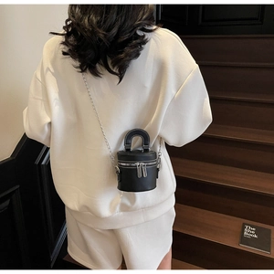 Détail du sac cylindre noir avec surpiqûres blanches et chaîne argentée sur modèle