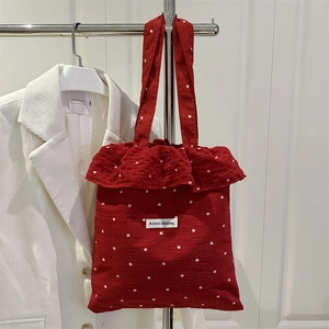Red floral tote bag with textured fabric and ruffle edge hanging on a clothes rack