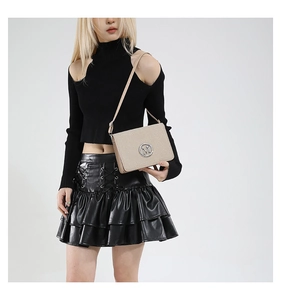 Detail of a beige structured camera bag with silver M logo on stylish black outfit